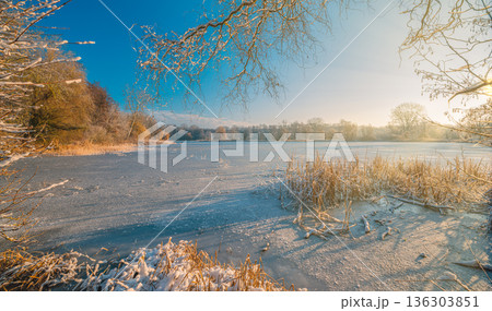 Frozen sunset lake landscape with warm sunlight. Tranquil winter nature scenery 136303851