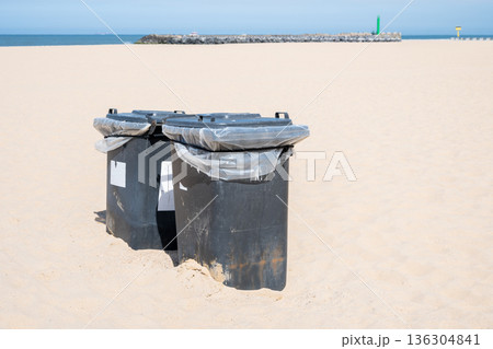 Green and black plastic waste containers buried in yellow sand on the beach. Ostend, Belgien. Green and black plastic waste containers buried in yellow sand on the beach. Ostend, Belgien. 136304841