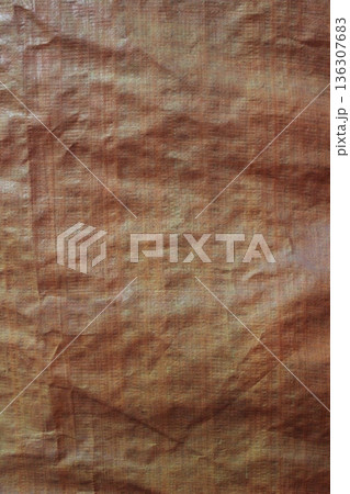 Detailed texture of brownish orange woven tarp fabric with creases and dense plastic fibers 136307683