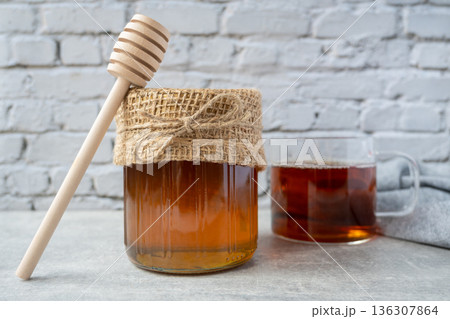 Honey jar with honeycomb, cap of tee and wood spoon stay on the table near napkin. 136307864