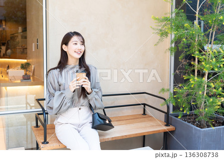 カフェの前のベンチに座り、テイクアウトのコーヒーを手に持つ若い女性 136308738