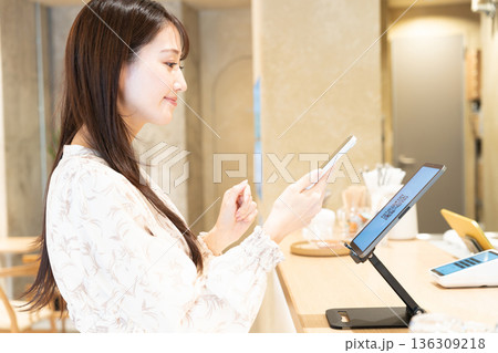 カフェでQRコードを読み取って会計をしようとしている若い女性 カフェでQRコードを読み取って会計をしようとしている若い女性 136309218