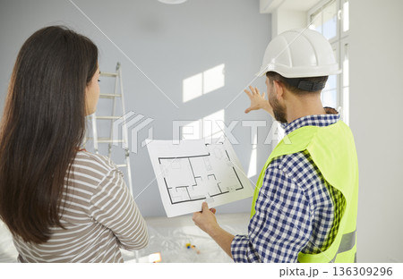 Architect, engineer or builder in uniform and helmet discusses construction plan with house owner 136309296