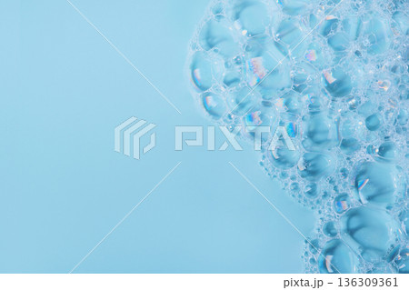 Soap bubbles forming a lather texture with light reflections on blue background 136309361