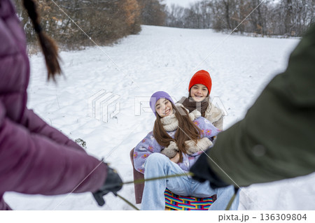 Parents pulling daughters on sled through winter landscape. Parents pulling daughters on sled through winter landscape. 136309804