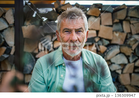 Older man with gray hair posing in front of wooden logs. Older man with gray hair posing in front of wooden logs. 136309947
