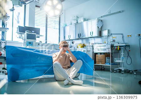 Worried teenage patient sitting alone on hospital floor, struggling with mental health issues. 136309975
