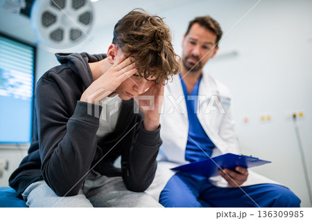 Depressed teenage patient sitting on hospital bed, talking with caring doctor. Depressed teenage patient sitting on hospital bed, talking with caring doctor. 136309985