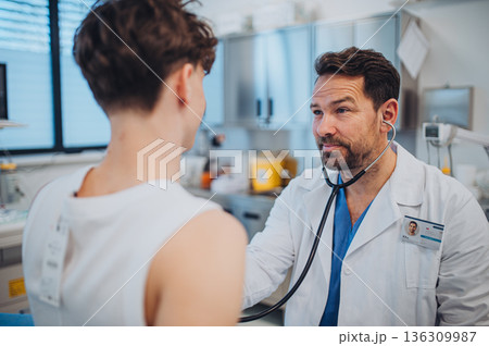Cardiologist examining adolescent patient with stethoscope in clinic. 136309987