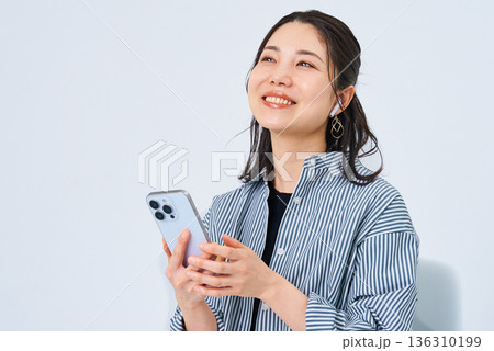 イヤホンを装着してスマートフォンを手にする若い女性 イヤホンを装着してスマートフォンを手にする若い女性 136310199