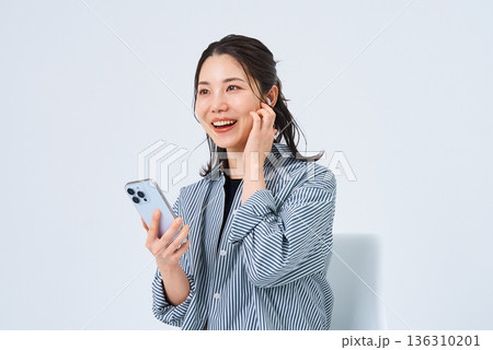 イヤホンを装着してスマートフォンを手にする若い女性 イヤホンを装着してスマートフォンを手にする若い女性 136310201