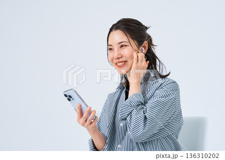 イヤホンを装着してスマートフォンを手にする若い女性 イヤホンを装着してスマートフォンを手にする若い女性 136310202
