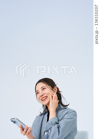 イヤホンを装着してスマートフォンを手にする若い女性 136310207