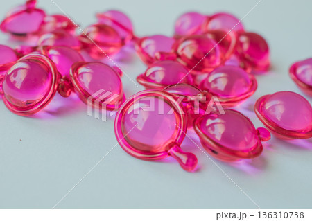 Close-up macro shot of many glossy pink hair treatment capsules. Focused foreground highlights the rich oil and reflective texture Close-up macro shot of many glossy pink hair treatment capsules. Focused foreground highlights the rich oil and reflective texture 136310738