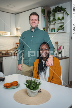 Interracial couple posing in kitchen, embracing, smiling at camera 136310883