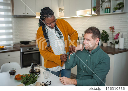 Female caregiver assisting man with dressing arm in kitchen 136310886