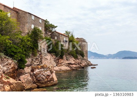 Coastal fortress-like stone buildings rise from a rocky cliff Coastal fortress-like stone buildings rise from a rocky cliff 136310983