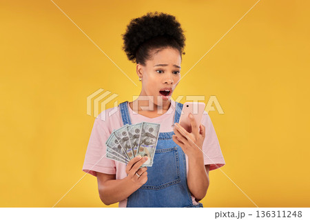Surprise, money and winner with black woman and phone in studio for success, prize or deal. Bonus, lottery and online payment with person and cash on yellow background for dollar, profit or giveaway 136311248