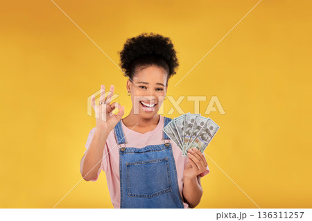 Okay, money and winner with portrait of black woman in studio for success, prize or achievement. Bonus, lottery and investment with person and cash on yellow background for dollar, profit or giveaway Okay, money and winner with portrait of black woman in studio for success, prize or achievement. Bonus, lottery and investment with person and cash on yellow background for dollar, profit or giveaway 136311257