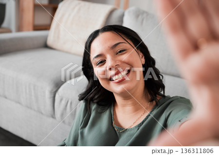 Selfie, happy and portrait of a woman in her living room relaxing, resting or chilling by the sofa. Happiness, smile and young female person from Mexico taking a picture at her modern home apartment. 136311806