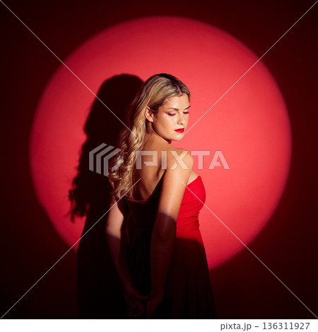 Beauty, spotlight and red with a model woman in studio on a dark background for classy elegance or style. Fashion, aesthetic and luxury with a confident young female person standing in a dress 136311927