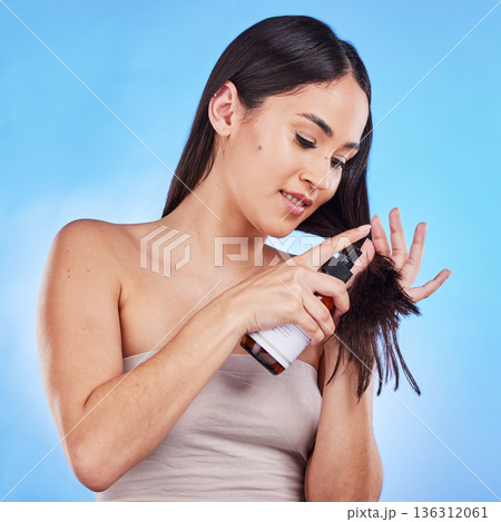 Woman, beauty and hair with spray for growth in blue studio background with luxury cosmetic. Shine, haircare and girl with keratin treatment with product for dry texture or repair with bottle. 136312061