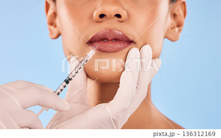 Lip filler, injection and beauty, woman and cosmetic surgery closeup and dermatology on blue background. Face, skincare and syringe, female model and doctor hands with liquid collagen in studio 136312169