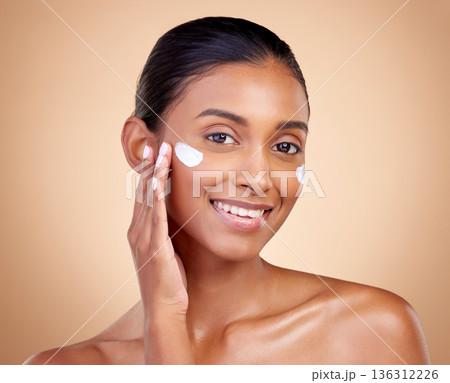 Face, cream and portrait of indian woman, skincare cosmetics and aesthetic dermatology on studio background. Happy young female model, lotion and facial sunscreen for clean beauty, glow and self care Face, cream and portrait of indian woman, skincare cosmetics and aesthetic dermatology on studio background. Happy young female model, lotion and facial sunscreen for clean beauty, glow and self care 136312226