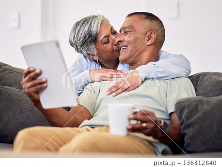 Senior couple, hug and tablet on sofa to relax with quality time in home with kiss during retirement. Couple, technology and embrace with elderly man or woman in living room together on couch. Senior couple, hug and tablet on sofa to relax with quality time in home with kiss during retirement. Couple, technology and embrace with elderly man or woman in living room together on couch. 136312840