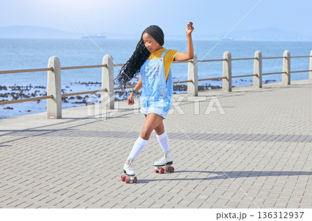 Roller skating, fun or freedom with a black woman by the sea, on the promenade for training or recreation. Beach, sports and a young female teenager in skates on the coast by the ocean or water Roller skating, fun or freedom with a black woman by the sea, on the promenade for training or recreation. Beach, sports and a young female teenager in skates on the coast by the ocean or water 136312937