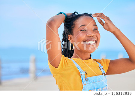 Portrait, smile and hair with a black woman on a blurred background by the ocean during summer vacation. Face, happy and braids with a young female person outdoor on the promenade for a holiday Portrait, smile and hair with a black woman on a blurred background by the ocean during summer vacation. Face, happy and braids with a young female person outdoor on the promenade for a holiday 136312939