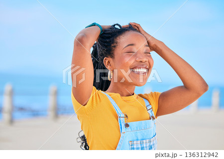 Face, smile and hair with a black woman on a blurred background by the ocean during summer vacation. Eyes closed, happy and braids with a young female person outdoor on the promenade for a holiday Face, smile and hair with a black woman on a blurred background by the ocean during summer vacation. Eyes closed, happy and braids with a young female person outdoor on the promenade for a holiday 136312942
