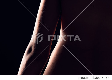 Beauty, body and person on black background for creative lighting, shadow and silhouette. Aesthetic, skincare and closeup of waist in dark studio with macro of skin for art deco, wellness and glow 136313058