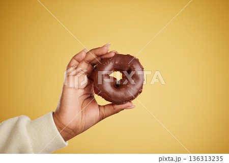 Hand, donut and chocolate dessert in studio for unhealthy eating, sugar or cake advertising. Closeup of a person with a doughnut on a yellow background for junk food, diet calories or fun emoji Hand, donut and chocolate dessert in studio for unhealthy eating, sugar or cake advertising. Closeup of a person with a doughnut on a yellow background for junk food, diet calories or fun emoji 136313235