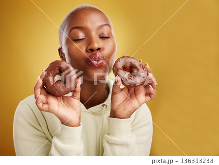 Face, kiss and donut with a black woman in studio on a golden background for candy or unhealthy eating. Pout, food and baking with a cute young female person holding sweet pastry for dessert Face, kiss and donut with a black woman in studio on a golden background for candy or unhealthy eating. Pout, food and baking with a cute young female person holding sweet pastry for dessert 136313238