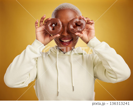 Face, chocolate and donut with a black woman in studio on a gold background for candy or unhealthy eating. Smile, food and baking with an excited young female person holding sweet pastry for dessert Face, chocolate and donut with a black woman in studio on a gold background for candy or unhealthy eating. Smile, food and baking with an excited young female person holding sweet pastry for dessert 136313241