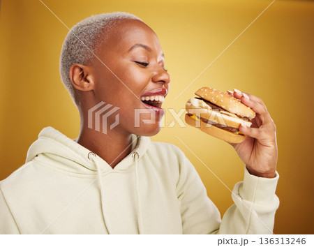 Burger, eating and young woman or student on studio, yellow background for restaurant, lunch and youth discount. Hungry and excited african person or customer experience, fast food and hamburger bite 136313246