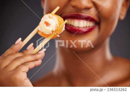Sushi, chopsticks and mouth of a woman in studio for healthy eating, salmon or food. Black female model with makeup and smile on a dark background for wellness, diet or seafood advertising in hand 136313262