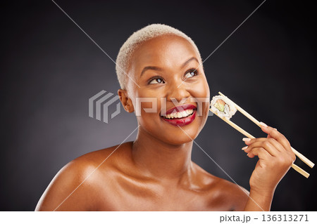 Thinking, face and woman with sushi and chopsticks in studio for healthy eating, beauty or food. Happy black female model with makeup idea on dark background for wellness, diet or seafood advertising 136313271