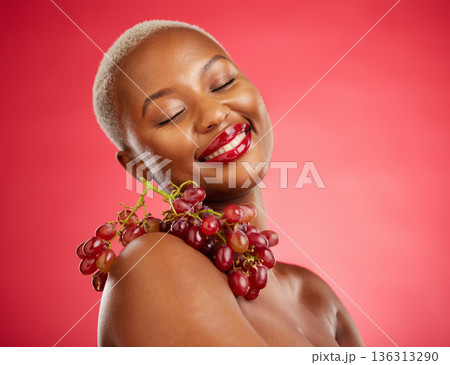Skincare, smile and grapes with a model black woman in studio on a red background for health or nutrition. Beauty, happy and fruit with a young female person posing for wellness, diet or detox 136313290
