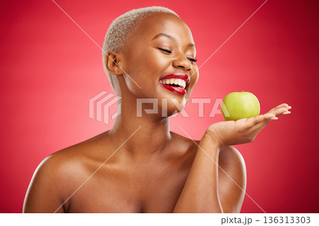 Happy black woman, apple and natural nutrition for diet, health and wellness against a red studio background. African female person smile and palm with organic green fruit for food, snack or meal 136313303