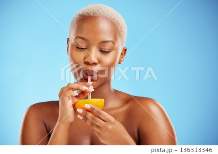 Black woman, vitamin C and drinking orange for diet or natural nutrition against a blue studio background. Calm African female person with citrus fruit, drink and straw for healthy wellness or juice Black woman, vitamin C and drinking orange for diet or natural nutrition against a blue studio background. Calm African female person with citrus fruit, drink and straw for healthy wellness or juice 136313346
