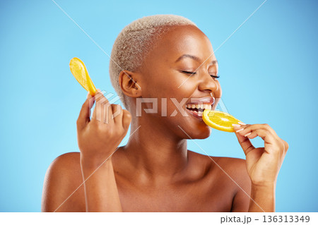 Orange, beauty and nutrition with a model black woman in studio on a blue background biting fruit. Food, skincare and natural with a happy young female person eating a snack for health or wellness Orange, beauty and nutrition with a model black woman in studio on a blue background biting fruit. Food, skincare and natural with a happy young female person eating a snack for health or wellness 136313349