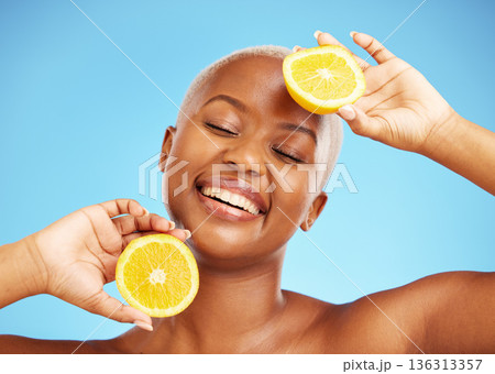 Orange, face and nutrition with a model black woman in studio on a blue background for treatment. Beauty, skincare and smile with a happy young person holding natural fruit for health or wellness 136313357