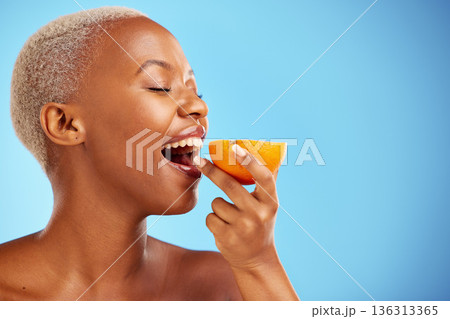 Orange, skincare and nutrition with a model black woman in studio on a blue background biting fruit. Food, beauty and natural with a happy young female person eating a snack for health or wellness Orange, skincare and nutrition with a model black woman in studio on a blue background biting fruit. Food, beauty and natural with a happy young female person eating a snack for health or wellness 136313365