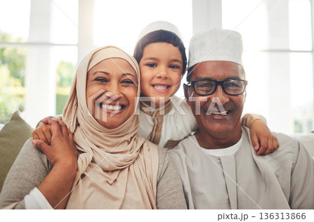 Portrait, Islam and grandparents with child for Eid with happy family in home with culture in Indonesia. Senior Muslim man, old woman in hijab and kid with smile on face on sofa together in lounge. Portrait, Islam and grandparents with child for Eid with happy family in home with culture in Indonesia. Senior Muslim man, old woman in hijab and kid with smile on face on sofa together in lounge. 136313866