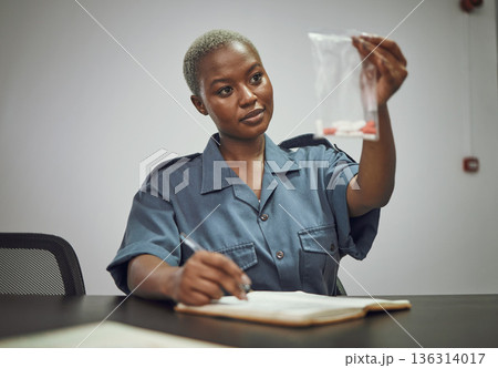 Black woman, drugs and writing police report with evidence from crime, investigation or search in room. African female person, law enforcement or officer holding illegal pills or trace from criminal Black woman, drugs and writing police report with evidence from crime, investigation or search in room. African female person, law enforcement or officer holding illegal pills or trace from criminal 136314017