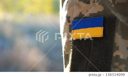 Close up of military blue-yellow chevron on shoulder of soldier at countryside. This emblem embodies the unbreakable spirit and pride of the ukrainian people. Concept of invasion resistance 136314099