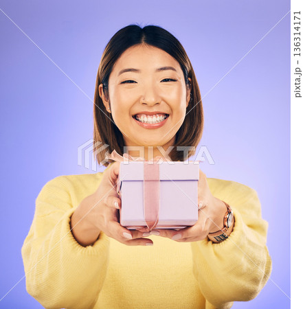 Portrait, smile and Asian woman with a gift, box and celebration against a studio background. Face, happy female person or model with happiness, present and giveaway with a ribbon, surprise and prize 136314171