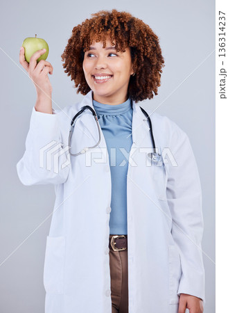 Doctor, woman and smile with apple in white background, studio and vitamin c wellness. Happy female medical worker, nutritionist and advice of green fruits for nutrition, healthy food and detox diet 136314237